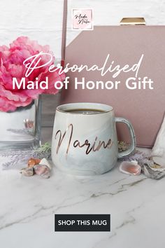 a personalized maid of honor gift mug next to a notepad and pink flowers