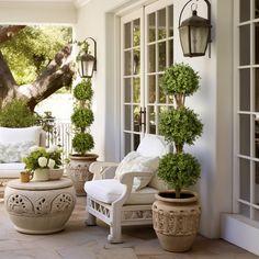 an outdoor living area with white furniture and potted plants on either side of the porch