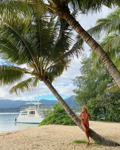 a woman in a red swimsuit standing on a palm tree next to the ocean