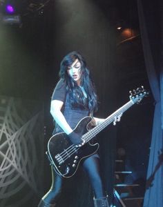 a woman with long black hair playing a bass guitar on stage at a music concert