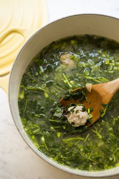 a wooden spoon in a pot filled with green vegetables and spinach soup on top of a marble countertop