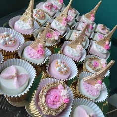 cupcakes with pink and gold decorations are arranged on a table in front of the eiffel tower