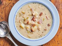 a bowl of soup with meat and potatoes on a wooden table next to a spoon