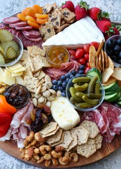 a platter with cheese, crackers, olives, tomatoes, grapes, nuts and fruit