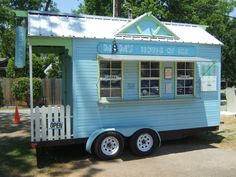 a small blue house on wheels parked in front of a fenced off area with trees