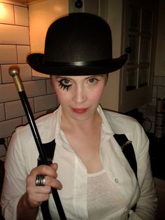 a woman in white shirt and black hat holding a stick with eyeliners on it