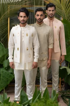 three men standing next to each other in front of plants