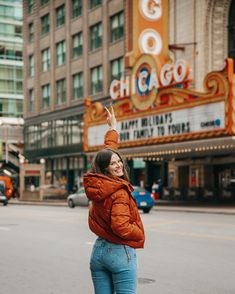 a woman standing in front of a movie marquee pointing at the sky with her hand up