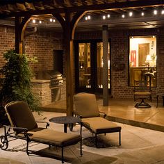 two chairs and a table on a patio at night with lights hanging from the ceiling