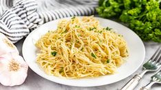 a white plate topped with pasta and parsley next to garlic, broccoli