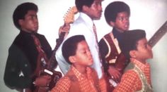 a group of young men standing next to each other with guitars in their hands and one man holding an electric guitar