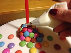 a person cutting into a cake with candy on it and a candle in the middle