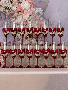 many wine glasses are lined up on a table with red satin ribbons and gold sequins