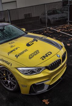 a yellow sports car parked in a parking lot next to a fence and some trees