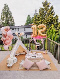 a teepee tent set up for a birthday party with pink and gold balloons in the air