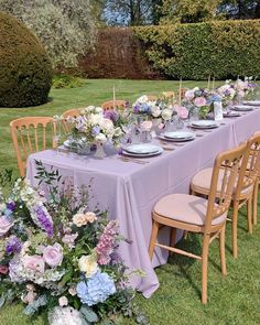 a long table with purple and white flowers is set up for an outdoor dinner party