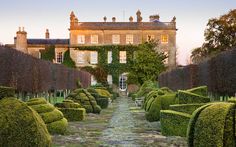 a large building with many hedges in front of it and a stone pathway leading to the entrance