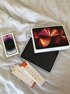 an apple laptop and other electronics on a bed