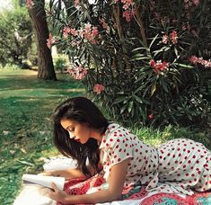 a woman laying on the ground reading a book with trees in the background and text that reads, at the park or in a garden