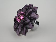 a purple flower ring with pink crystals on it's center and silver band, against a gray background