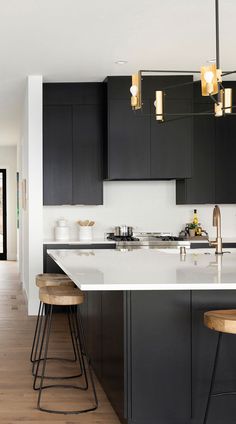 a kitchen with black cabinets and stools in front of an island countertop that has two bar stools on it