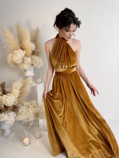 a woman in a gold dress is standing next to some vases and dried flowers