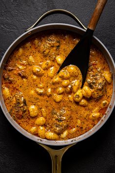 a pan filled with meatballs and sauce on top of a black table next to a wooden spoon