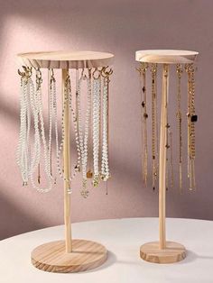 two wooden jewelry stands on top of a white table next to each other with gold chains hanging from them