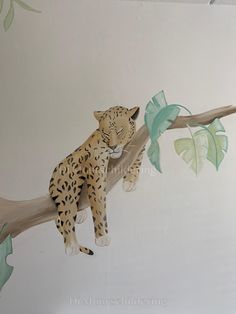 a painting of a leopard sitting on a tree branch with leaves painted on the wall behind it