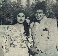 a man and woman standing next to each other in front of some trees on a sunny day