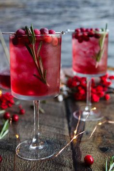 two glasses filled with cranberry shrub and garnished with rosemary, sitting on a wooden table