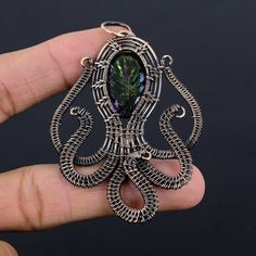 a hand holding an intricately designed pendant with a green crystal stone in the center