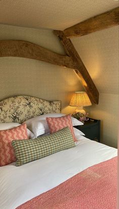 a bed with pink and green pillows in a bedroom next to a wooden beamed ceiling