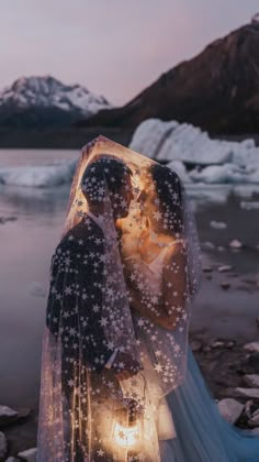 a bride and groom standing next to each other in front of the water at sunset