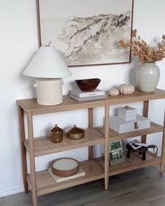 a shelf with some books and vases on it in front of a large painting