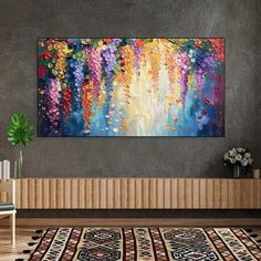 a large painting hanging on the wall above a rug in a room with a wooden table