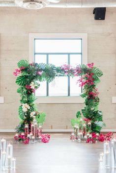 a table with flowers and candles on it in front of a large window that is decorated with greenery