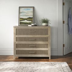 a dresser with a painting on top of it next to a rug and potted plant