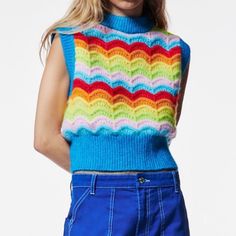 a woman is wearing a multicolored sweater and blue shorts with her hands on her hips