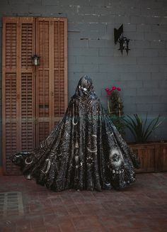 a woman in a black cloak is standing on a brick floor next to a door