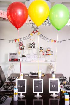 three balloons are in the air above a table with black chairs and plates on it