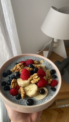 a bowl filled with fruit and nuts on top of a table next to a lamp