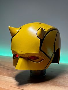 a yellow cat mask with red eyes sits on top of a wooden table in front of a green background