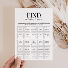 a hand holding up a printable game for the wedding party, with feathers in the background