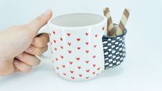 a hand holding a coffee mug with two matches in it and another cup that has hearts on it