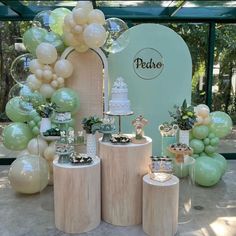 a table topped with lots of balloons and cake on top of wooden pedestals in front of a sign