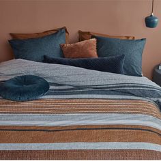 a bed with blue and brown striped comforter next to a lamp on the wall