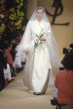 a woman in a white wedding dress and veil walking down the runway at a fashion show