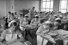 an old black and white photo of women in uniforms sitting at desks with books