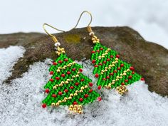 a pair of green and red beaded christmas tree earrings sitting on top of snow